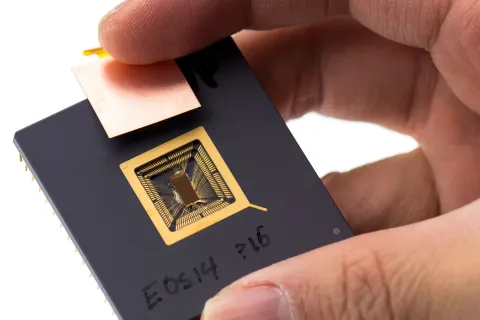 一隻手捏著黑色陶瓷封裝的 RISC-V 原型晶片，中央露出金色打線的晶粒